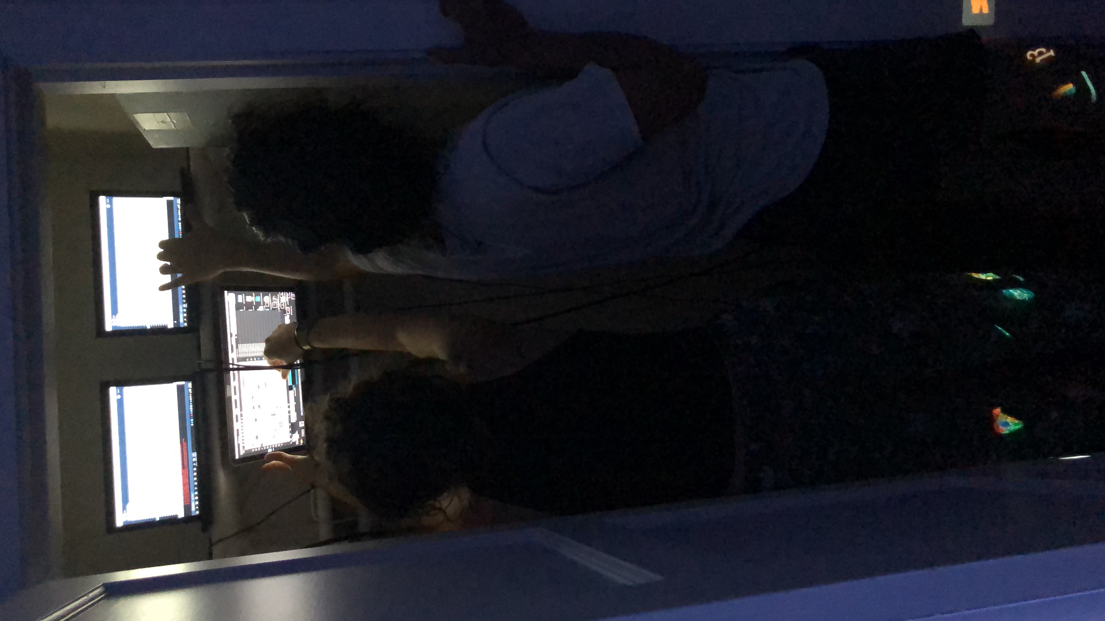 two people reaching into a small closet to adjust programs running on three laptops.